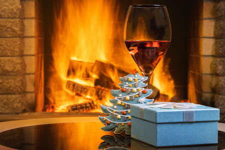 Christmas eve. Gift box and a glass of wine near cozy fireplace, in country house.の写真素材