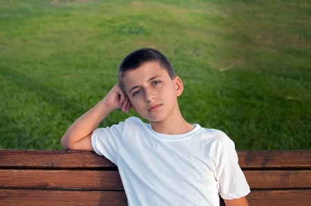 Boy sitting on a park bench with green meadow on the background .の写真素材