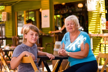 Boy with his grandmother in a cafe in outdoor restaurant on summer day .