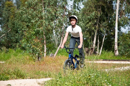 Teenager riding a bike on road through forest  