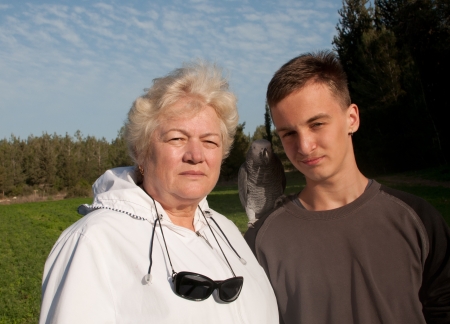 Elderly woman and a teenage boy with a parrot on a background of parkの写真素材