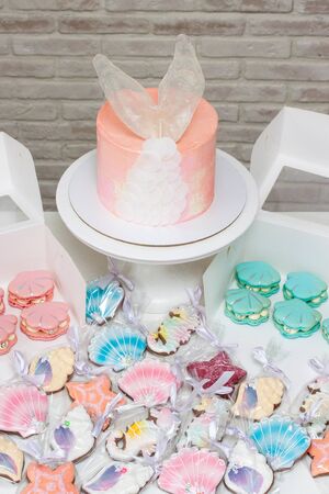 Mermaid theme candy bar with pink cake with fish tail, french macaroons, soft pastel pink, peach and...