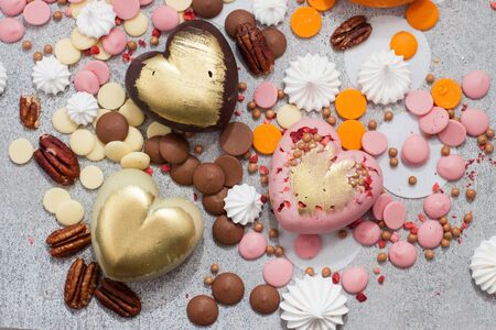 Assorted pink, orange, brown and green chocolate hearts with meringues, pecan nuts and chocolate dropsの写真素材