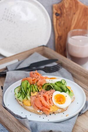 Sandwich with toast bread, smoked salmon, cream cheese, sliced cucumber and boiled eggs on white plate.の写真素材