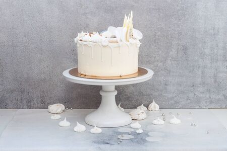 Elegant white wedding cake with chocolate decoration, meringues and macaroons on grey background.