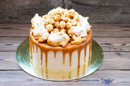 Homemade salted caramel cake with caramel sauce and caramel popcorn on wooden background