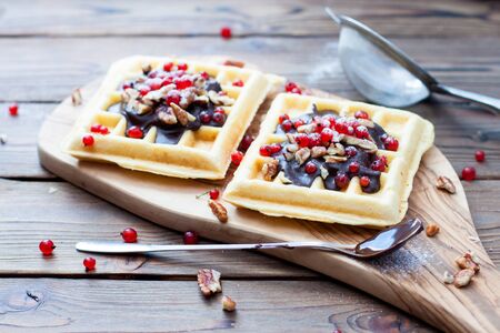 Belgian waffles with chocolate sauce, frozen berries, nuts and sugar powder on wooden platter. Rustic wooden background.の写真素材