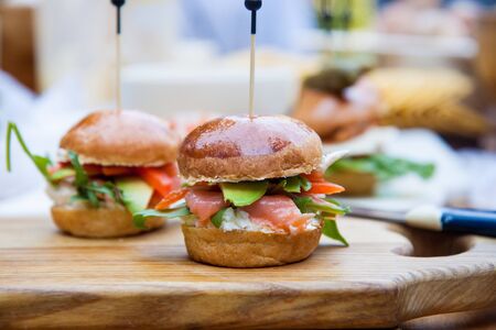 Burger with cream cheese, salted salmon, cale, avocado on wheat bun. Rustic background.