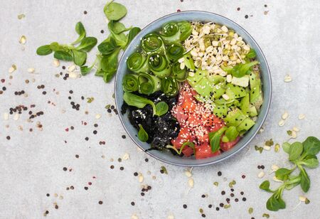 Poke bowl with smoked salmon, cucumber, avocado, sea kale, bean sprouts, baby spinach, sesame and herbs. Grey background, copy space.の写真素材