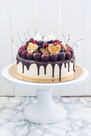 Vanilla cheesecake decorated with melted dark chocolate, fresh berries, cherries, chocolate hearts and meringues. White rustic background.の写真素材