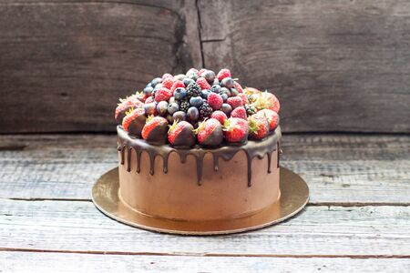 Chocolate brownie cake with fresh summer berries. Decorated with raspberries, strawberries, blueberries dipped into melted chocolate. Rustic background.の写真素材