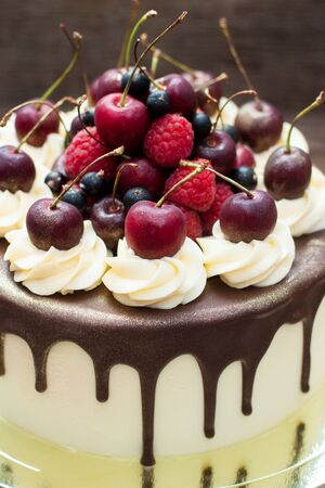 Homemade cake with melted chocolate decorated with whipped cream and fresh cheries on top. Rustic background.の写真素材