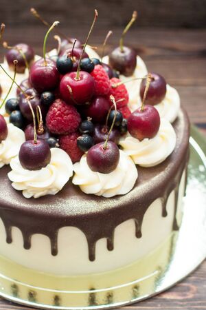 Homemade cake with melted chocolate decorated with whipped cream and fresh cheries on top. Rustic...