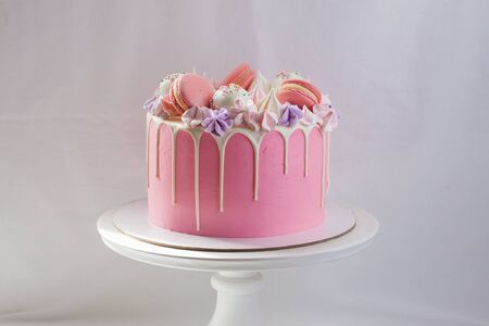 Tender pink cake decorated with melted white chocolate, macaroons, meringues, cake pops and candies...