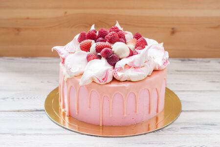 Pink cheese cake with melted chocolate, meringues, fresh raspberries and strawberries. Wooden background.の写真素材