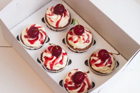 Vanilla cupcakes in gift box with berry sauce, whipped cream and fresh cherries on top. Selective focus.の写真素材