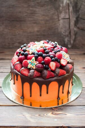 Bright red birthday cake with chocolate, fresh strawberry, raspberry, blueberry, cherry. Rustic background.の写真素材