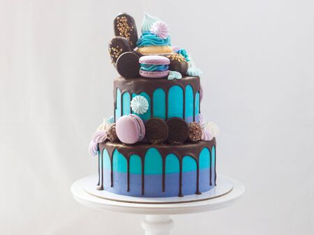 Tiered blue cake decorated with dark chocolate, cupcake, cookies, macaroons, meringues