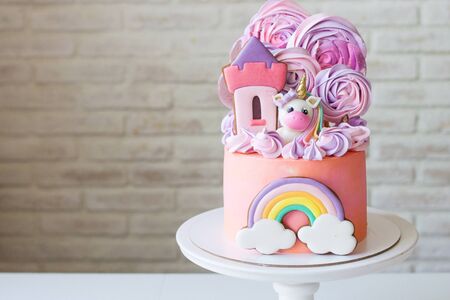 Cute pink birthday cake for a little girl with fondant unicorn, gingerbread princess castle, rainbow and meringue clouds.の写真素材