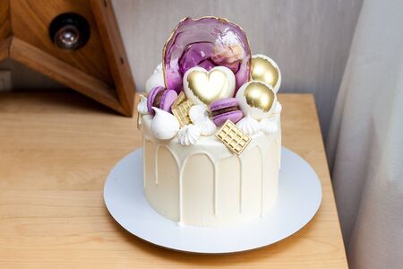 Modern elegant birthday cake with melted white chocolate, golden heart and chocolate balls,...