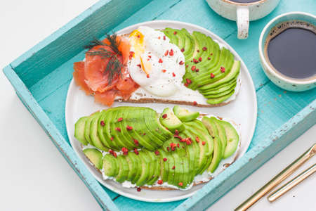 Bruschetta with salted salmon, chopped avocado, pepper and poached egg on a white plate on a...