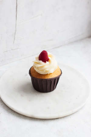 Vanilla cupcake with cream cheese frosting and fresh raspberry on gray backgroundの写真素材