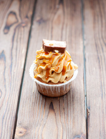 Delicious chocolate cupcakes with peanut butter frosting, chocolate bites and salted caramel sauce on rustic wooden backgroundの写真素材