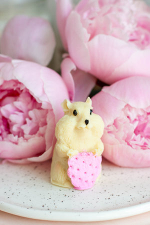Edible hamster made of white chocolate holding a strawberry. Peonies and candles on the backgroundの写真素材