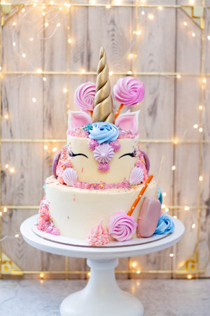 Two layered birthday unicorn cake with golden fondant horn, eyelashes and cream cheese frosting on...
