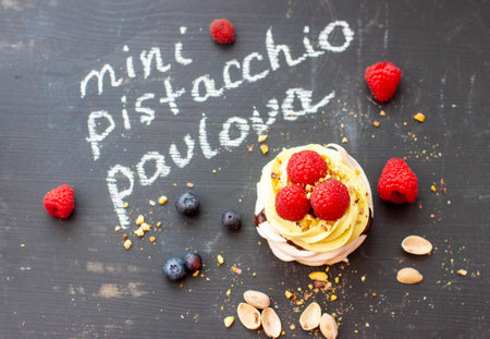 Close up of mini pistachio pavlova cake with fresh raspberries and blueberries on black chalk boardの写真素材