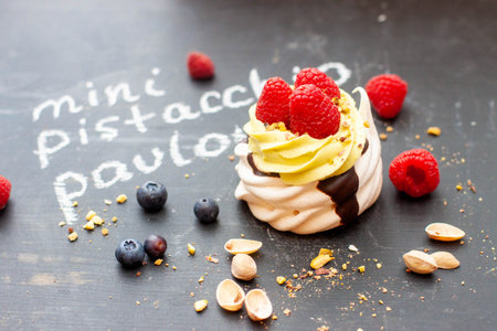 Close up of mini pistachio pavlova cake with fresh raspberries and blueberries on black chalk boardの写真素材