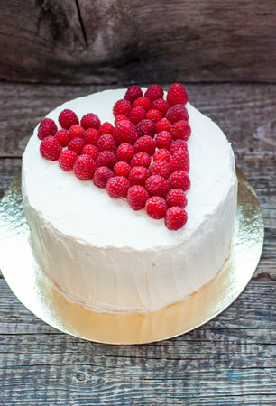 Elegant white cake with raspberry heart for St. Valentine's Day, Mother's Day, or Birthday, decorated with fresh berries sugar on wooden backgroundの写真素材