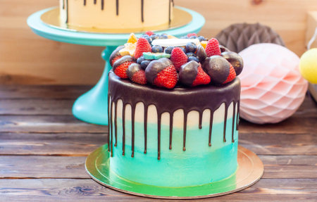 Two Birthday Drip Cakes with chocolate ganache and fresh berries, wooden background