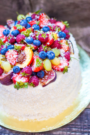 Coconut cake with a pile of fresh peaches, apples, raspberries, blueberries and nuts on wooden...