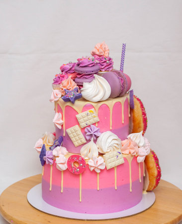 Pink ombre birthday cake with donuts, meringues and chocolate on neutral background. Cupcake on the...