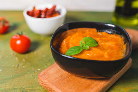 Pumpkin baked with dried and fresh tomatoes. Dark ceramic plate with pumpkin puree, basil leaf on...