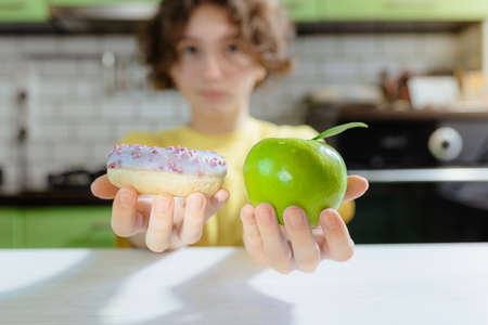 Choosing healthy between eating and junk food. Difficult to choose concept of healthy eating when woman holds green apple and donut with calorie bomb in her hands. Healthy food for teenagersの写真素材