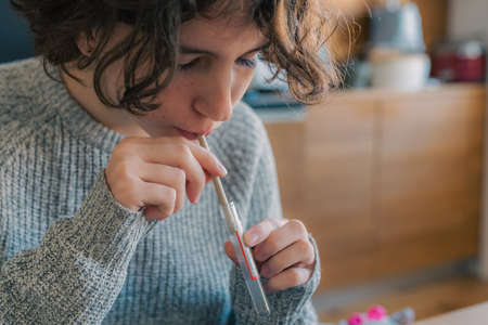 Collection of saliva test  at home. teenager girl with brown curly hair collects saliva in test tube, preventive test  at home.の写真素材