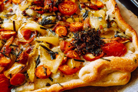 Spicy pie with vegetables, mushrooms, carrots, spinach and cheese on baking paper on light...