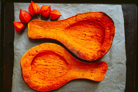 Baked pear-shaped Butternut pumpkin cut into two symmetrical halves, on baking sheet. Vegetarian baked rustic food, bright orange vegetable, pumpkin soup ingredientの写真素材