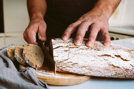 Close-up of a male hands cutting bread on a wooden boardの写真素材