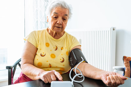 elderly woman with hypertension measures her blood pressure at home. Sad overweight mature lady measures blood pressure with tonometer. Daily health check.の写真素材
