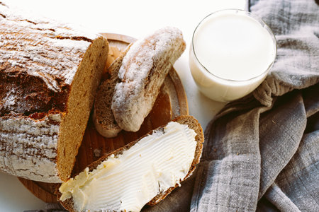 slice of rustic homemade rye flour bread buttered and glass of milk. country food, snack, freshly baked rye bread with butter and milkの写真素材