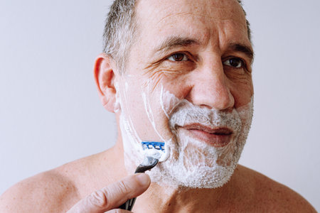 face of middle-aged man close-up, brown eyes, with stubble on face, lathered with shaving foam,...
