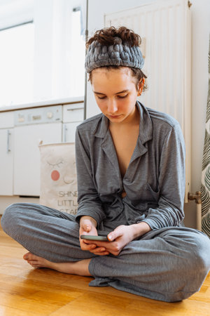 teenager checks notifications on smartphone, blogs on Internet, connected to Wi-Fi, sits on floorの写真素材