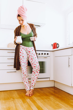 Young woman in pajamas with cup of coffee in the kitchenの写真素材
