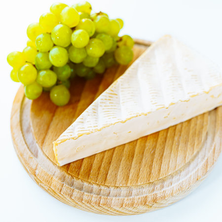 Brie cheese on wooden round board with bunch of white grapesの写真素材