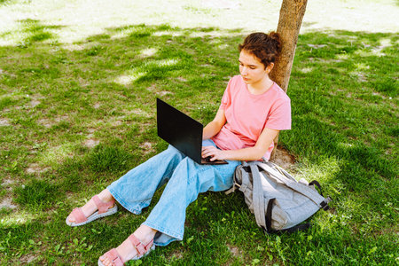 Young woman sitting on the grass in the park and working on laptopの写真素材