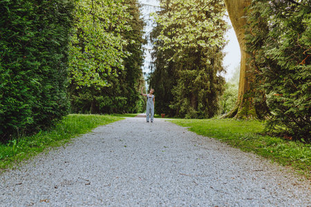 Silhouette of young girl on alley of natural park with large tall trees. Little man in big world of natureの写真素材