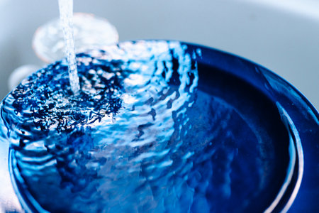 flow of water from water faucet with splashes on surface of blue plateの写真素材